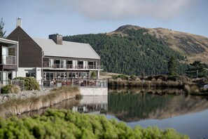 A modern building with a large patio area, a mountain in the background, and a body of water in the foreground. - Peppers Bluewater Resort (Lake Tekapo)