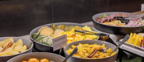 A buffet with various dishes including sliced peaches, oranges, and other fruits.