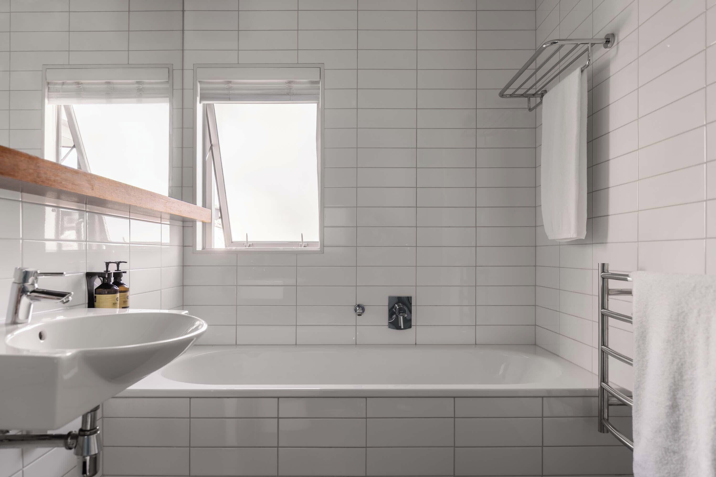 A bathroom with a white sink, a bathtub, and a window.