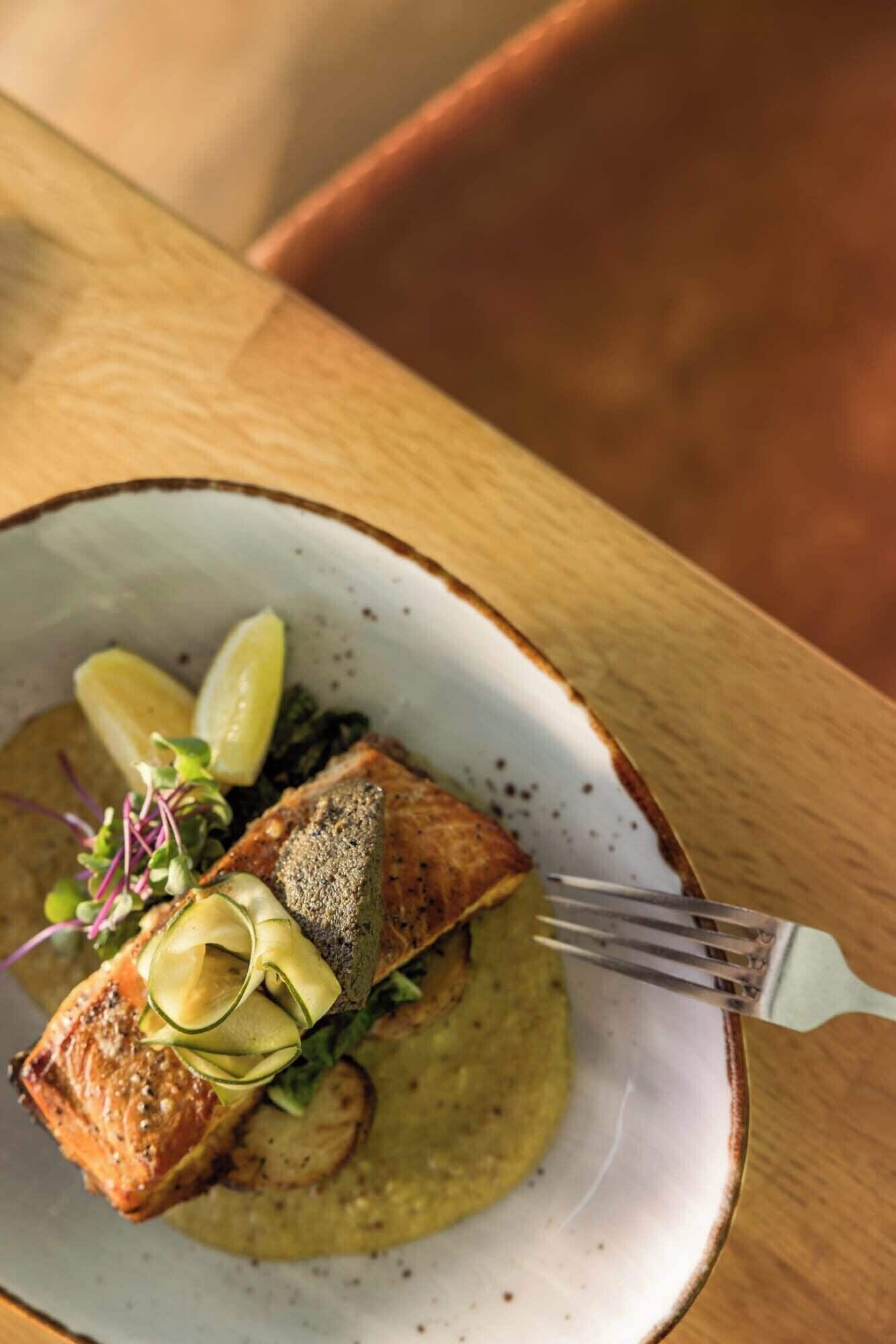 A plate of food with salmon, lemon slices, and greens on a ceramic plate.