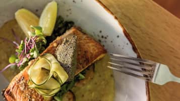 A plate of food with salmon, lemon slices, and greens on a ceramic plate.