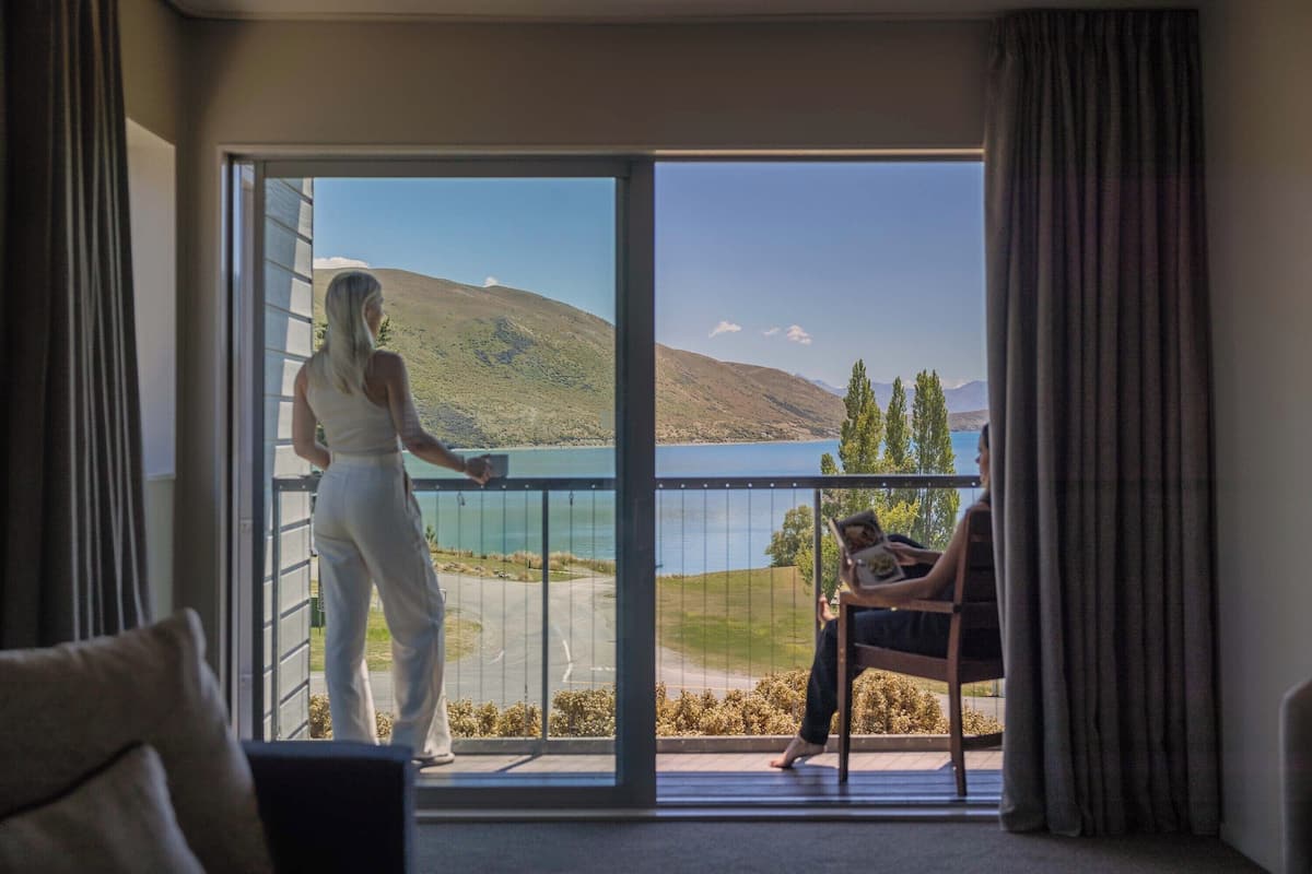 Habitación con balcón con vistas a un lago y colinas.