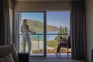 Habitación con balcón con vistas a un lago y colinas.