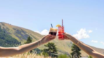 Dos manos sosteniendo vasos con bebidas con montañas al fondo.