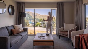 Ett modernt hotellrum med en stor skjutdörr i glas som leder ut till en vacker utsikt, en soffa, en fåtölj och ett soffbord med en fjärrkontroll och glas på.