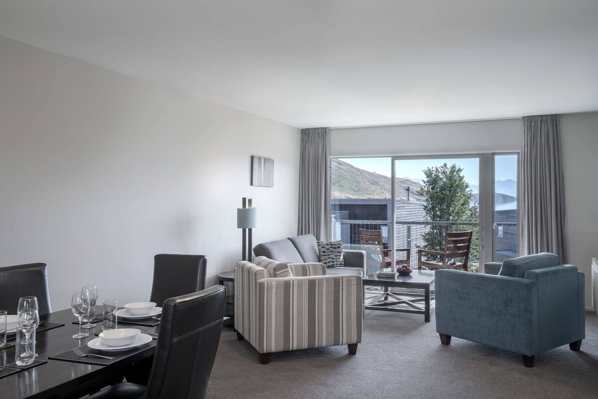 Una habitación de hotel moderna con zona de comedor, sofá y vistas a la montaña.