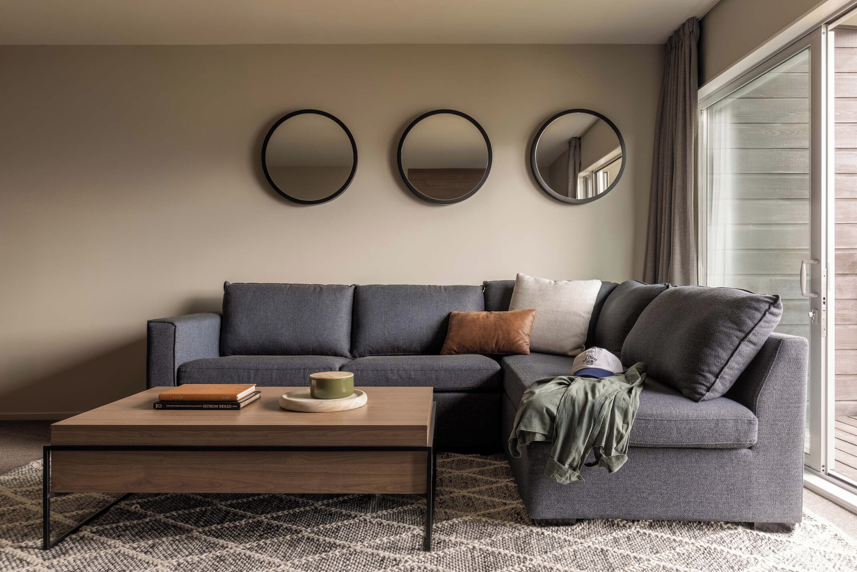 A modern living room with a grey sofa, a wooden coffee table, and three round mirrors on the wall.