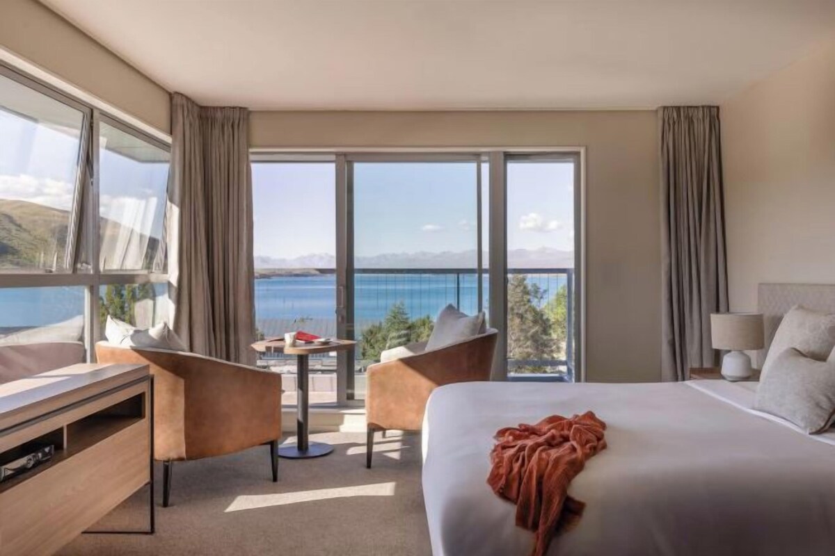 A hotel room with a large bed, a desk, a chair, and a view of the sea.