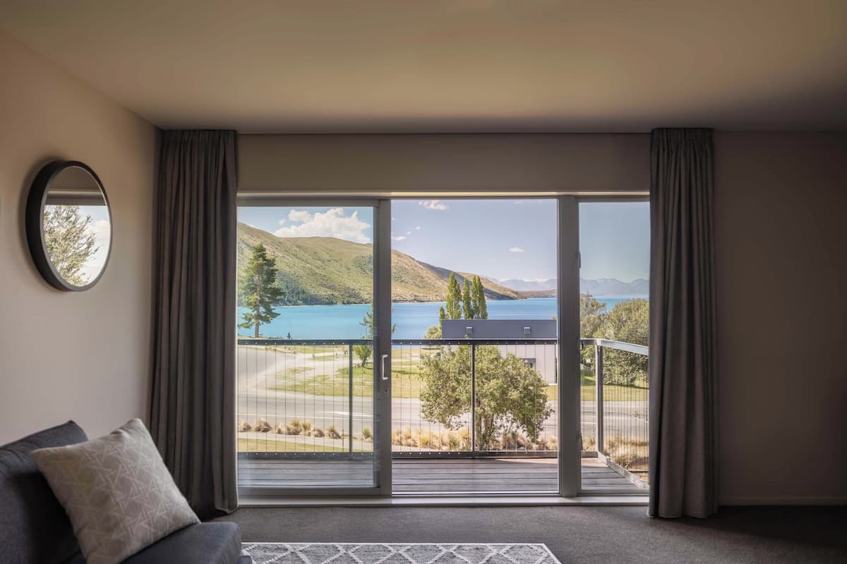 Una habitación con un amplio ventanal corredera que da a un balcón con vistas a un lago y montañas.