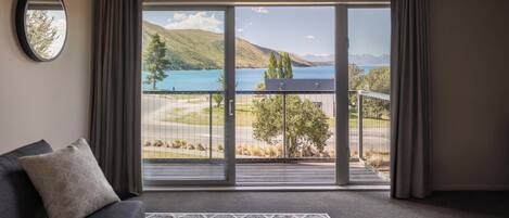 A room with a large sliding glass door leading to a balcony with a view of a lake and mountains.