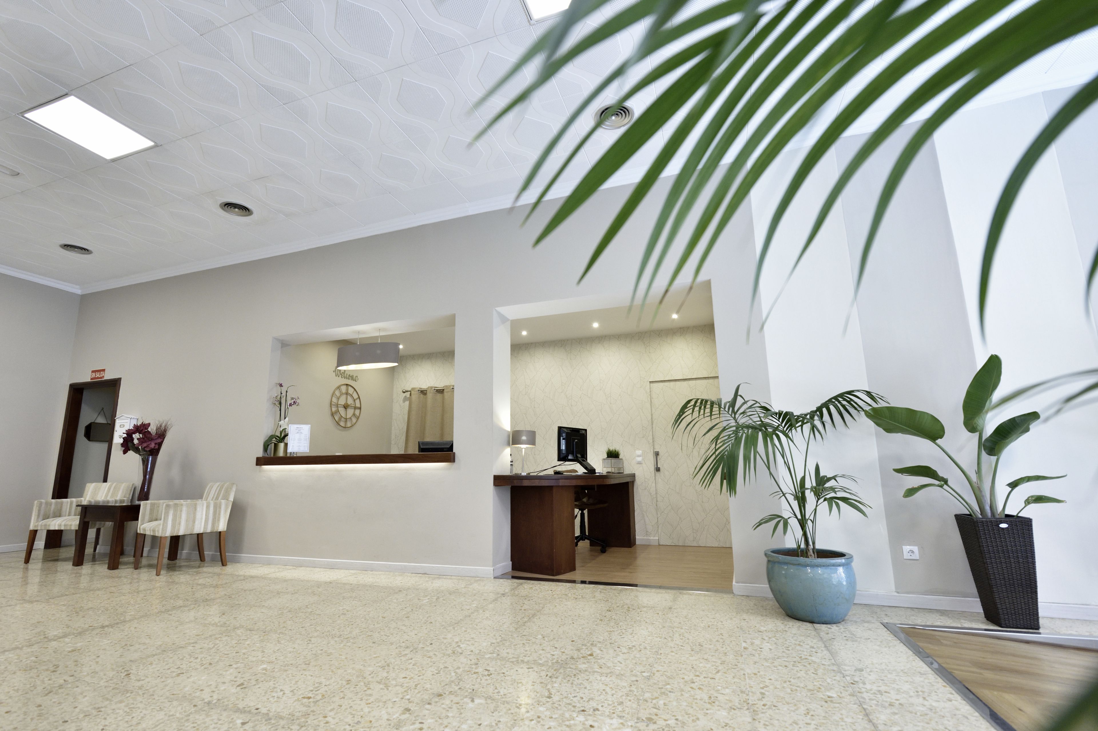 Um lobby de hotel moderno com balcão de recepção, área de estar e plantas em vasos.
