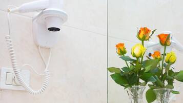 A hairdryer mounted on a wall with a coiled cord, and a mirror reflecting roses in vases.