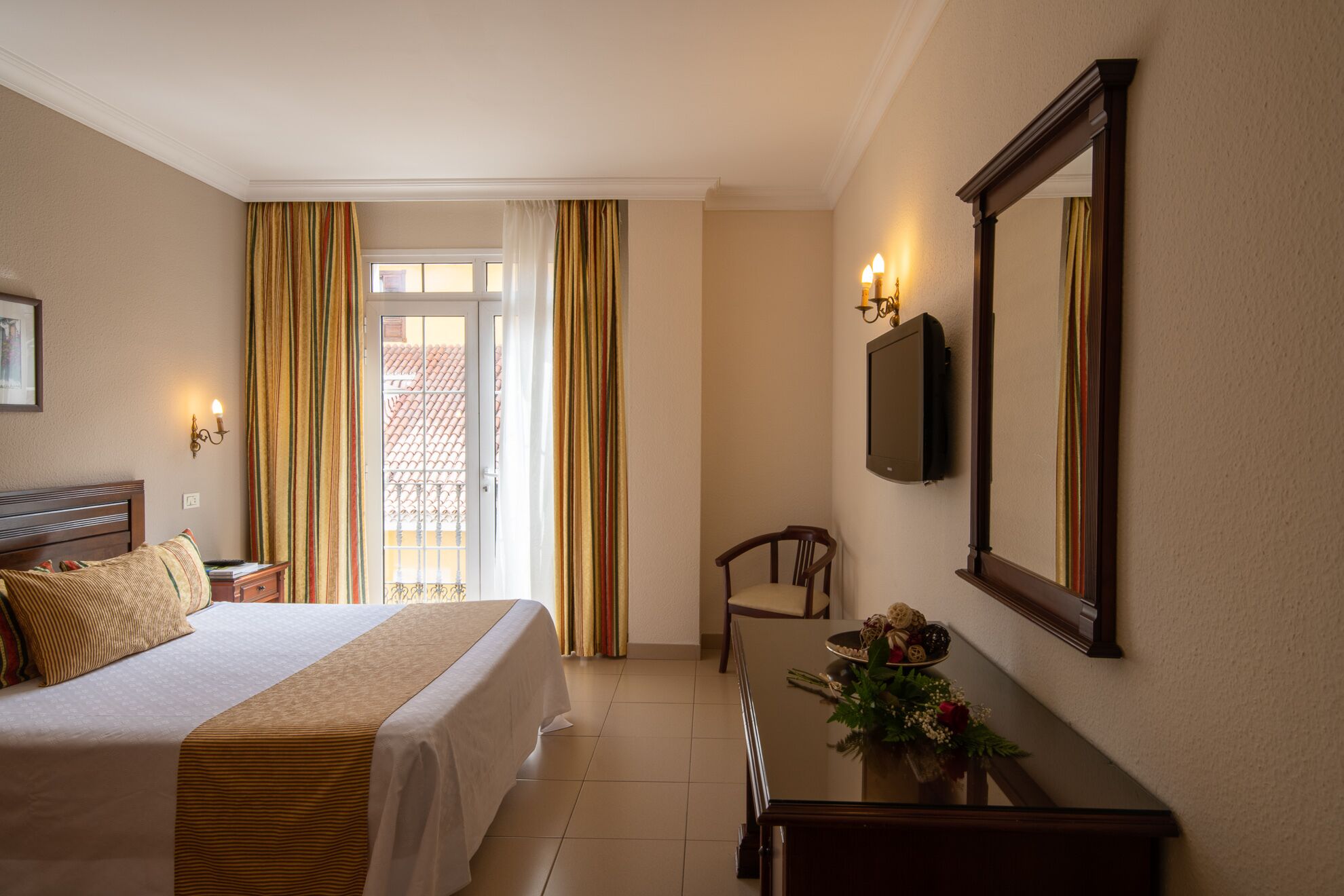 A hotel room with a bed, a desk, a chair, a mirror, and a window with curtains.