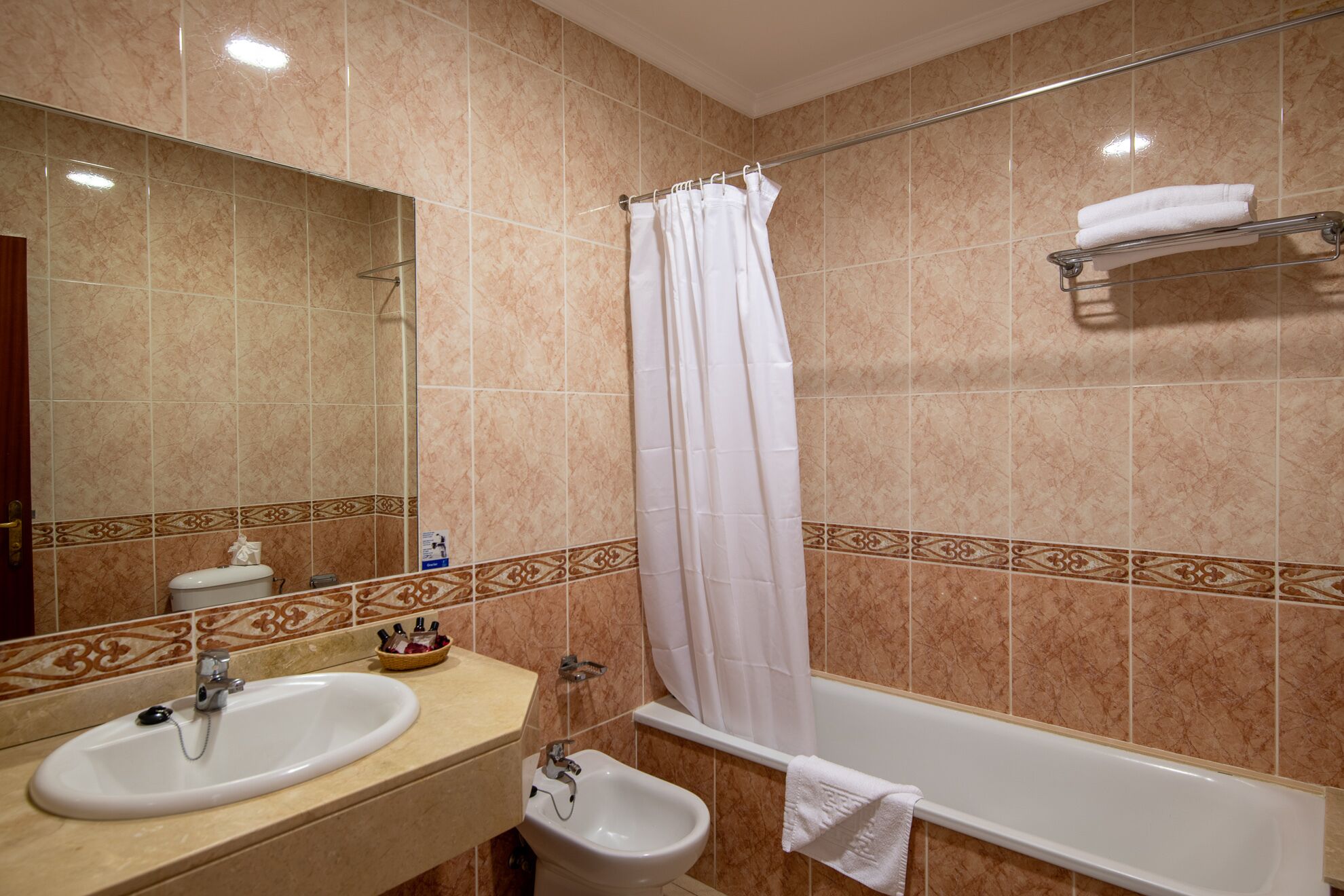 A bathroom with a bathtub, a shower curtain, a sink, and a bidet.