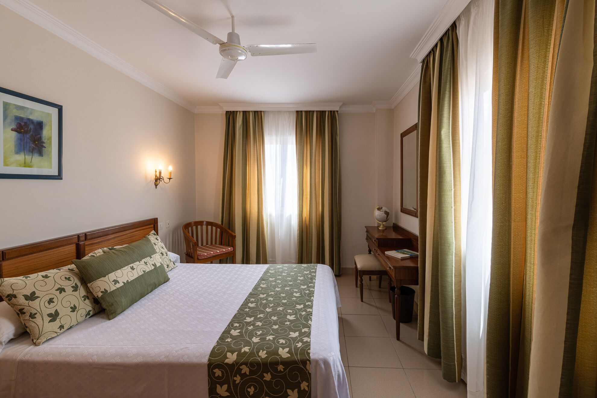 A hotel room with a bed, a chair, a desk, a globe, and curtains.