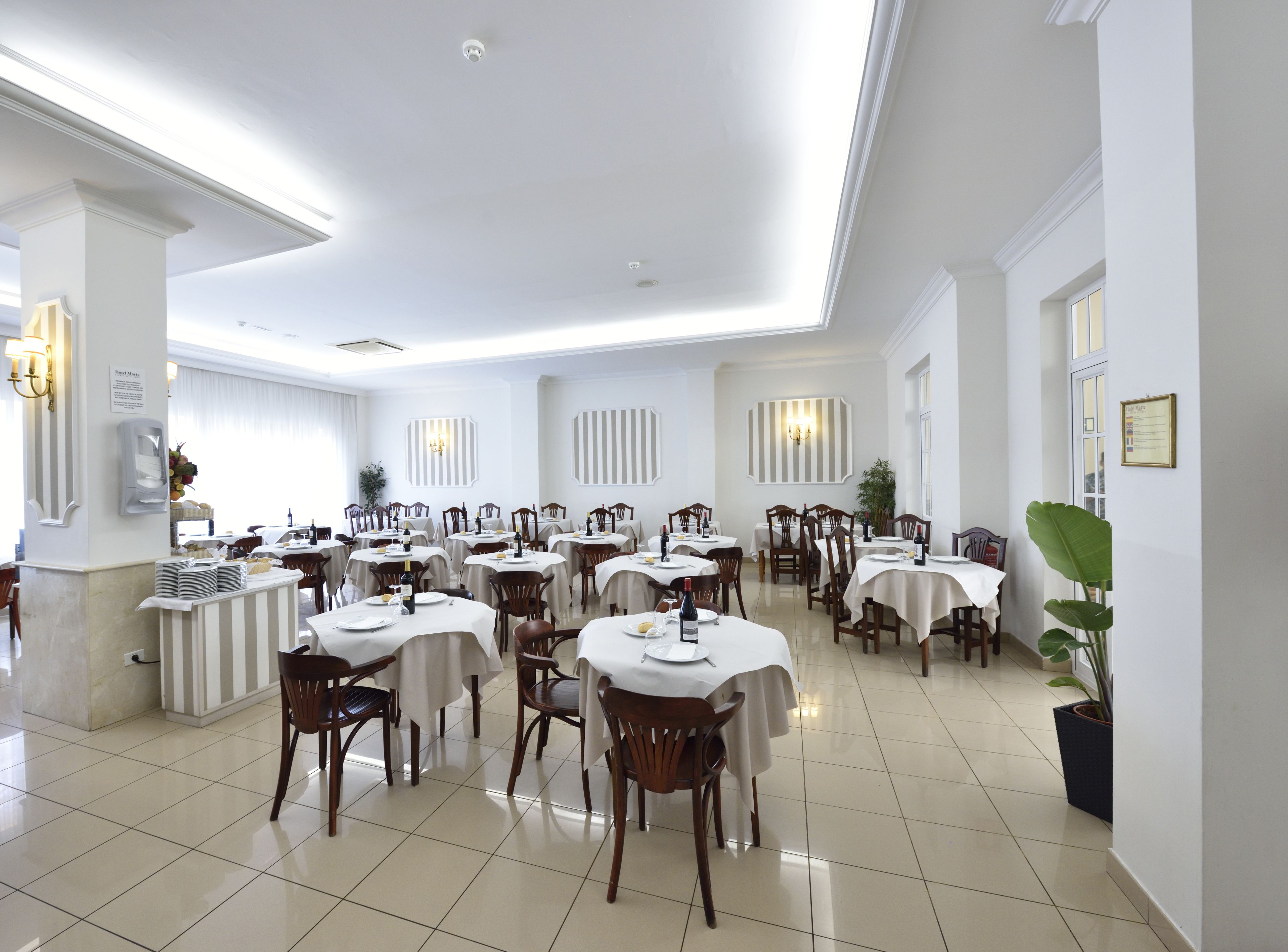 Un comedor de hotel con varias mesas y sillas, una estación de buffet y un mostrador de recepción.