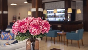 Un hall con zona de bar, asientos y un jarrón de flores rosas.