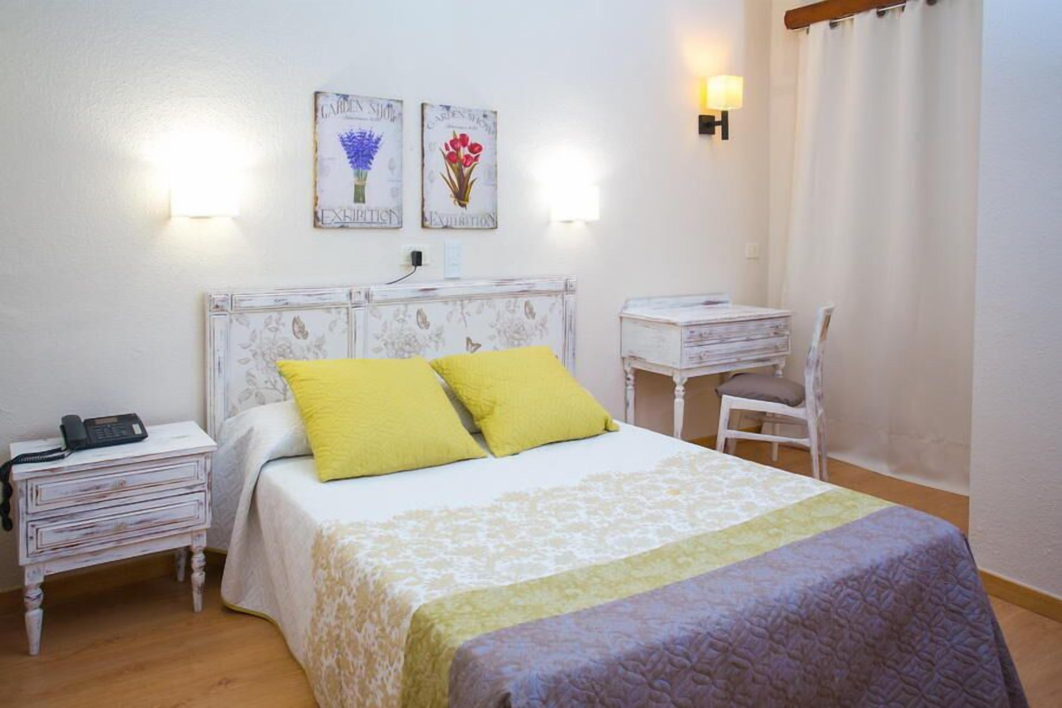 A bedroom with a bed, bedside table, lamp, and a desk with a chair.