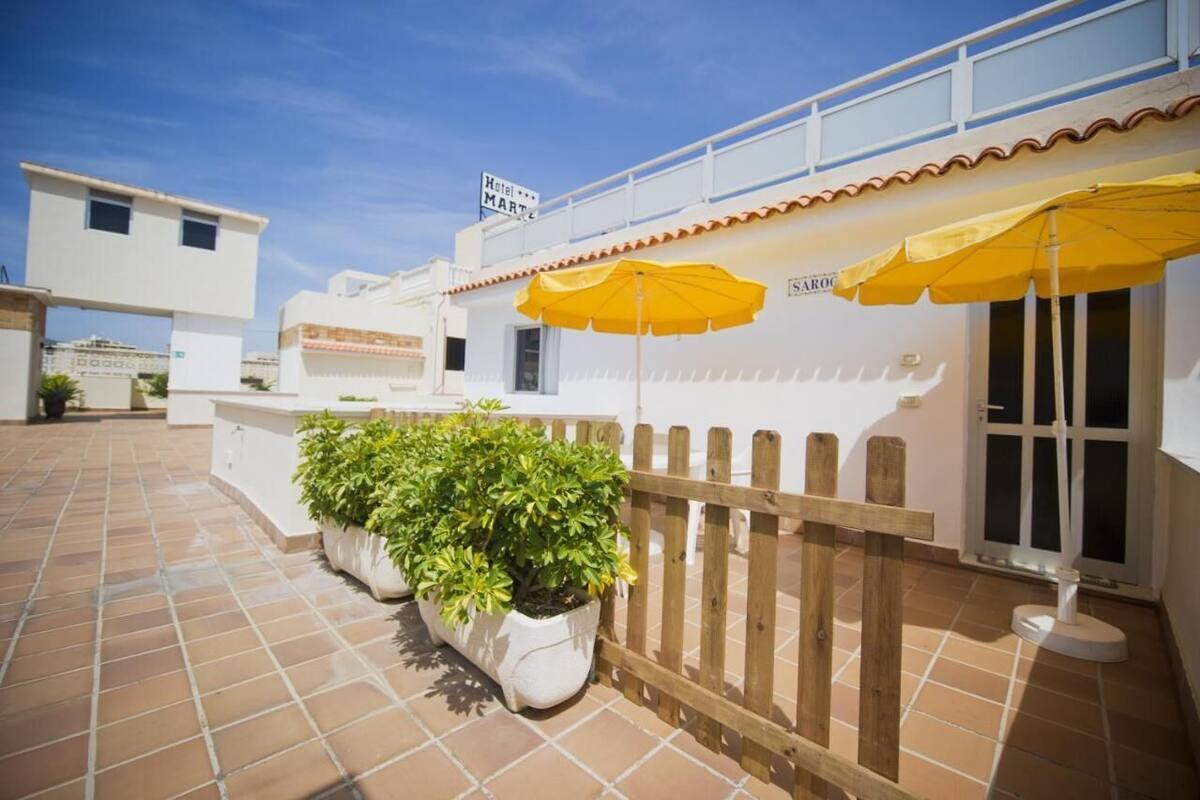 A hotel exterior with a tiled patio, yellow umbrellas, and potted plants.