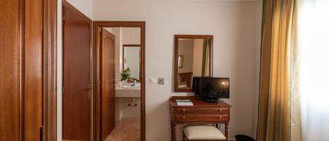 Una habitación de hotel con un escritorio de madera, televisor, cama y baño visible a través de una puerta abierta.