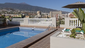 Una piscina en la azotea con vista a un paisaje urbano y montañas al fondo.