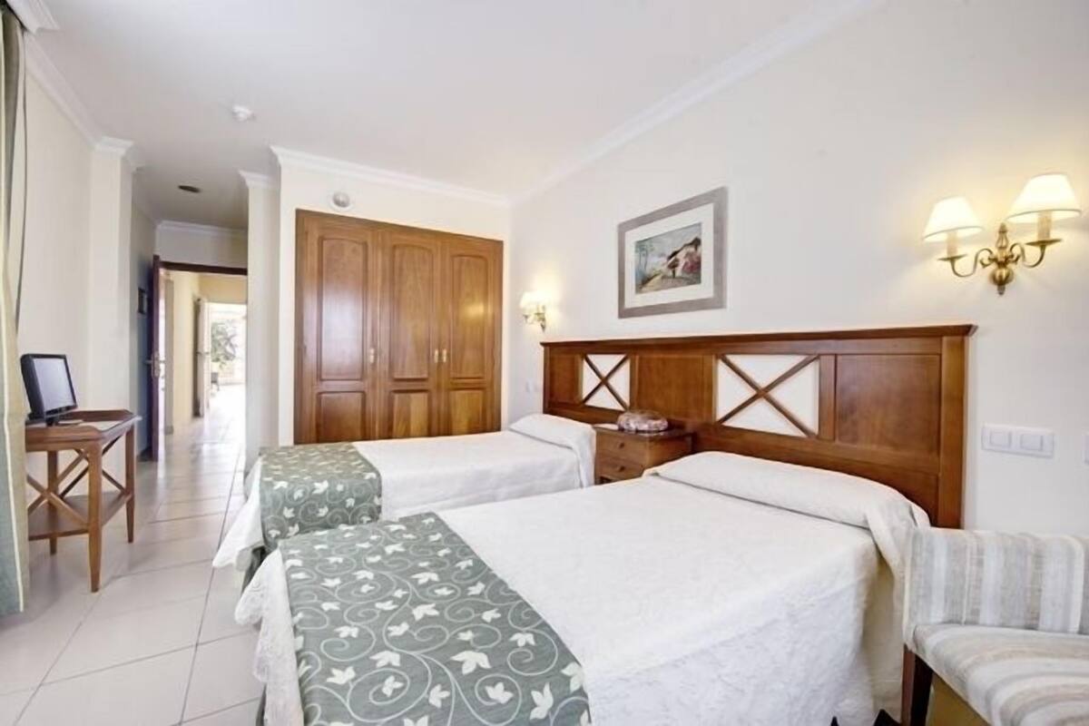 A hotel room with two beds, wooden headboards, a desk with a computer, and a chair.