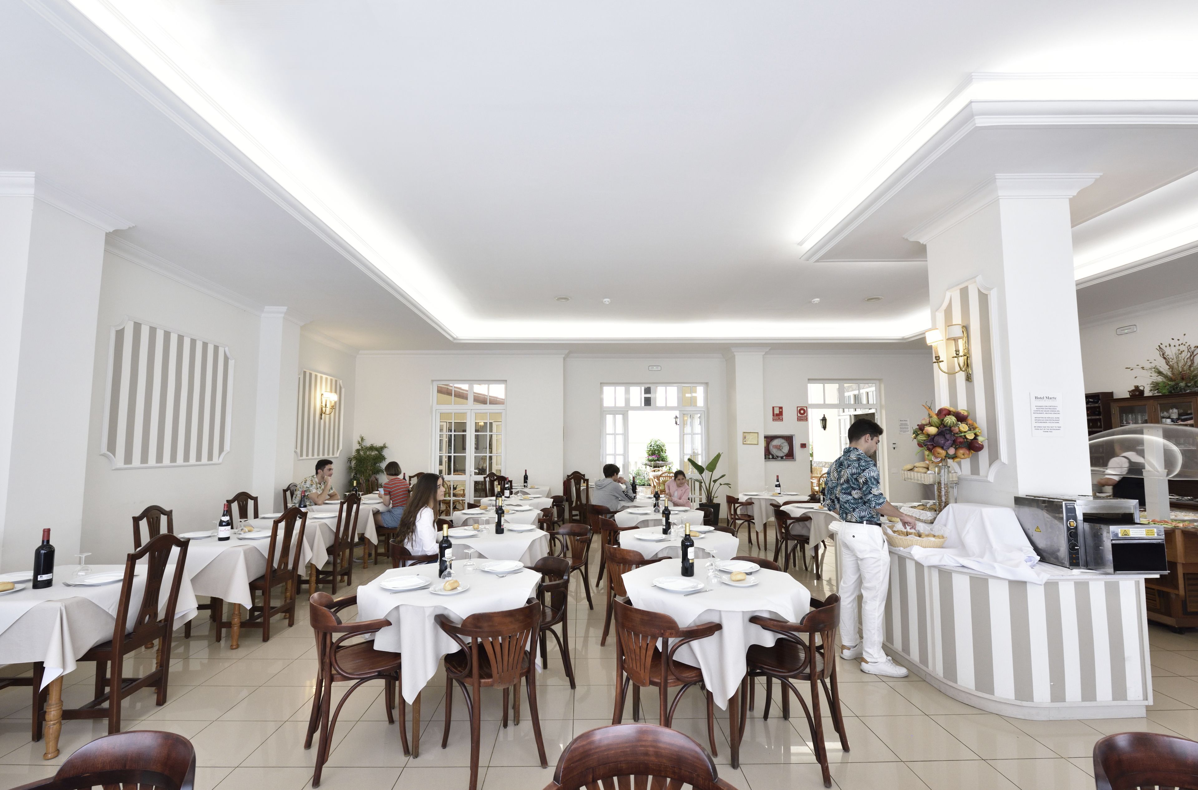 Un amplio comedor con varias mesas y sillas, una barra de buffet y un mostrador de recepción.