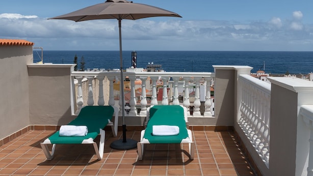 Un balcón con dos sillones de jardín verdes, un paraguas grande y vista al mar.