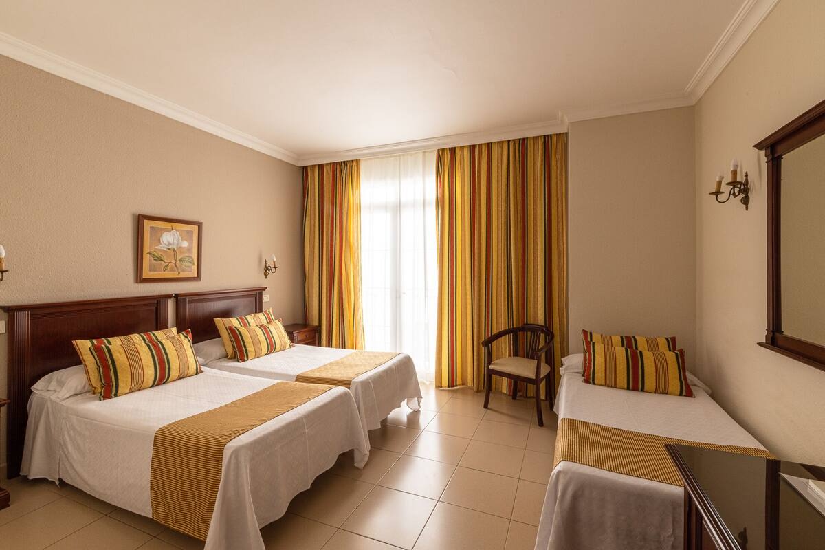 A hotel room with two beds, a chair, a desk, and a large window with curtains.