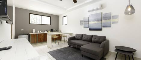 A modern living room with a sectional sofa, a dining area with a kitchen in the background, and artwork on the walls.