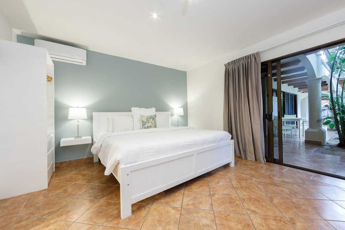 Un dormitorio con cama, dos lámparas de noche, un armario blanco y un ventanal corredero que da a un espacio exterior.
