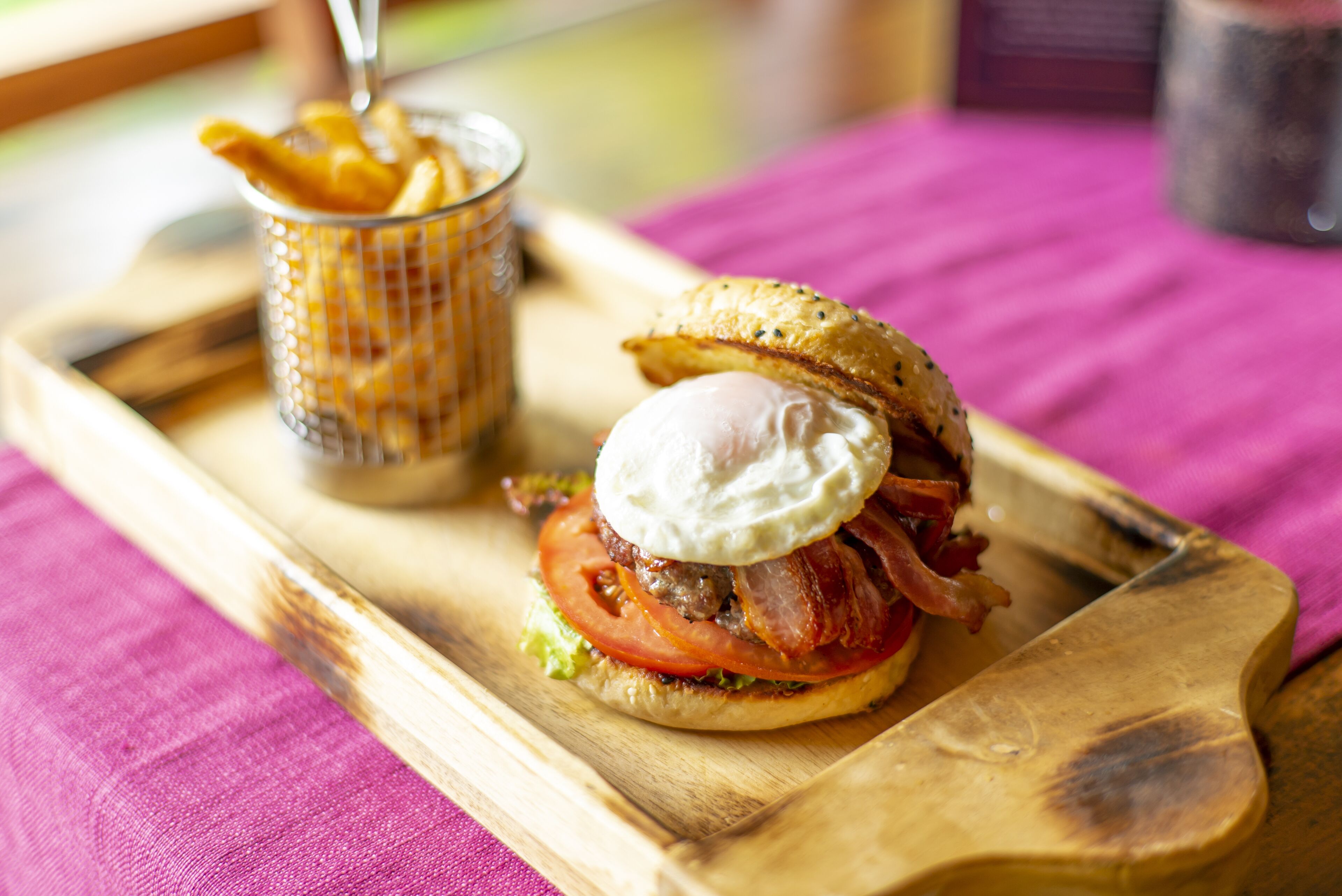 A breakfast sandwich on a wooden board with a side of fries.