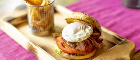 A breakfast sandwich on a wooden board with a side of fries.