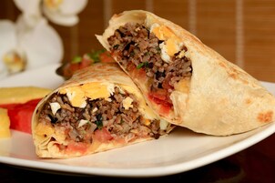 Un burrito con arroz, carne y vegetales en un plato.