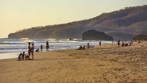 A beach with people, including children, and a surfboard. - RipJack Inn (Cabo Velas)