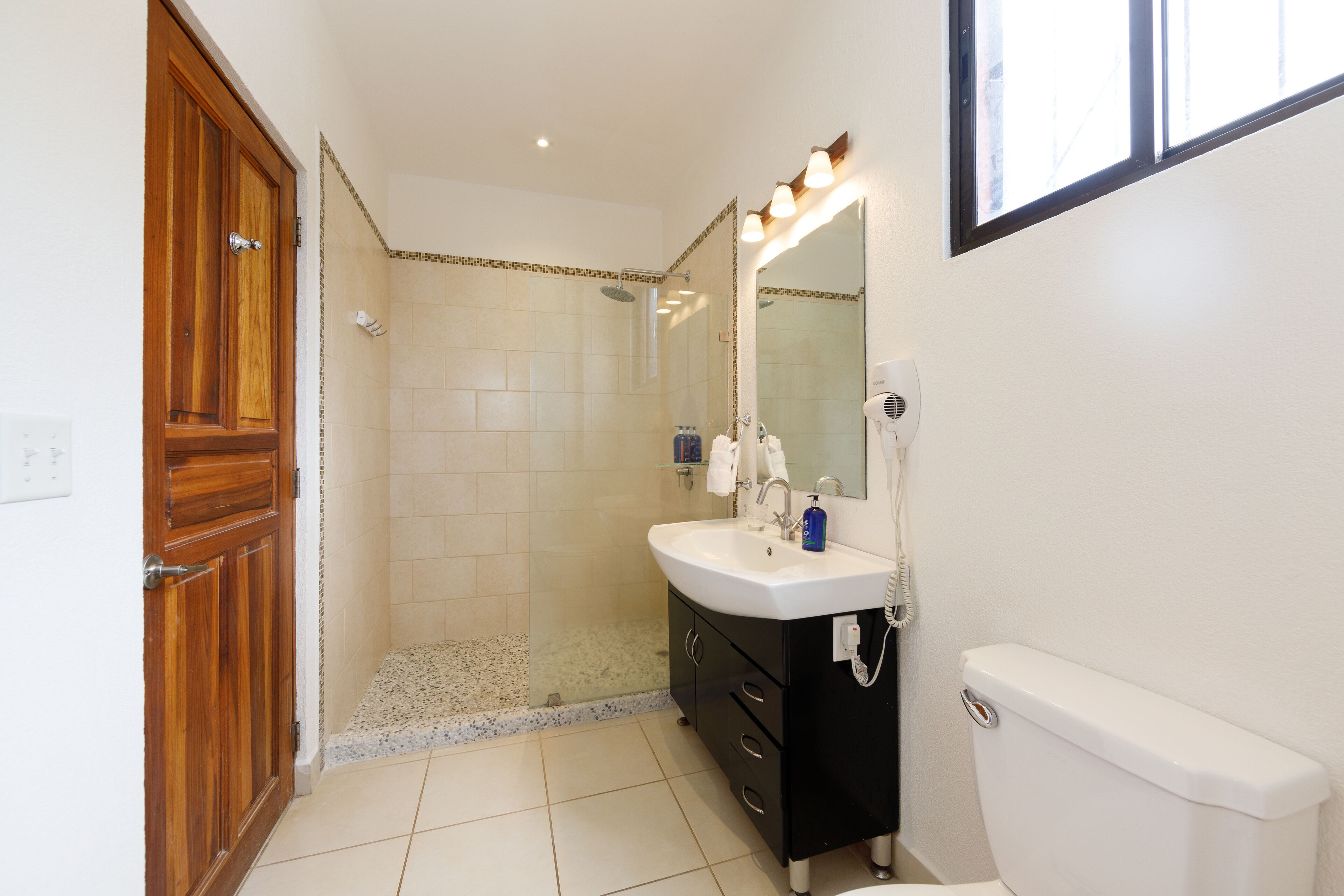 A bathroom with a wooden door, a shower, a sink with a mirror, and a toilet.