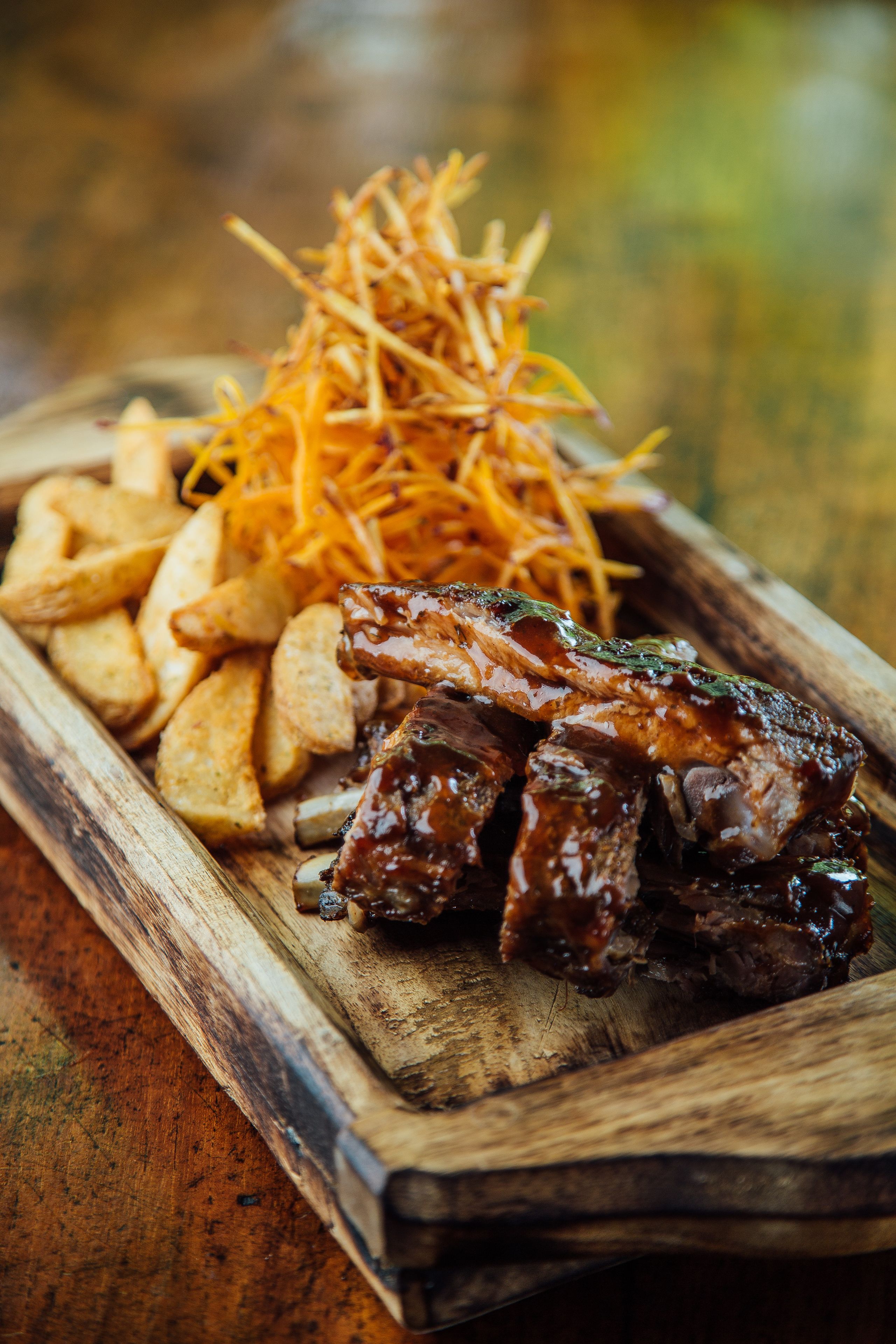 A wooden serving board with grilled meat, fries, and a side of shredded cheese.