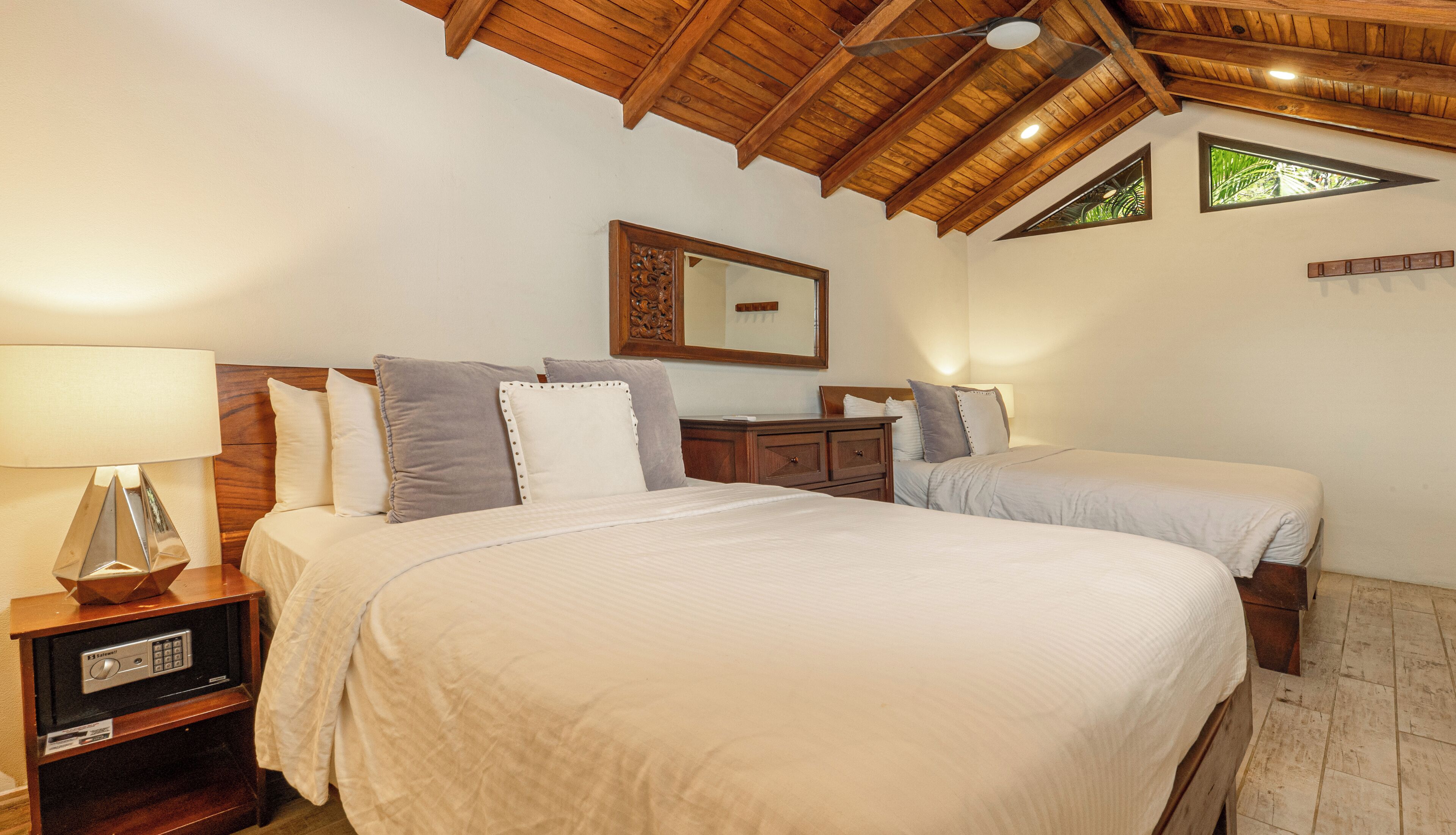 A bedroom with a large bed, a smaller bed, a nightstand with a lamp, a dresser, and a ceiling fan.