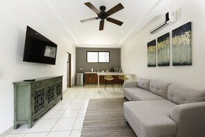 A modern living room with a flat-screen TV, a ceiling fan, and a dining area with a kitchen counter and chairs. - RipJack Inn (Cabo Velas)