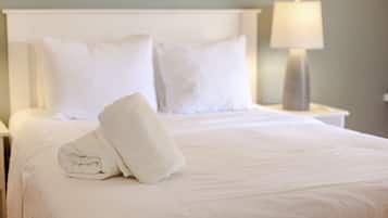 A neatly made bed with white linens and pillows, a folded towel on the bed, and a bedside lamp on the nightstand.