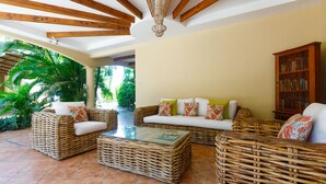 A spacious living area with wicker furniture, a glass coffee table, and a bookshelf. - RipJack Inn (Cabo Velas)