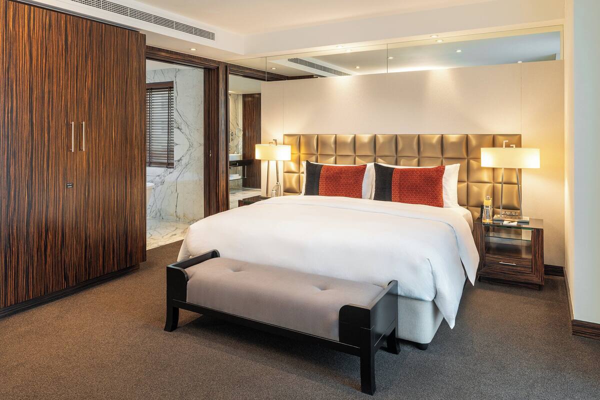Ein Hotelzimmer mit einem großen Bett, zwei Nachttischlampen, einer Bank, einem Kleiderschrank und einer Marmorwand.