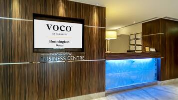 A reception desk with a wooden panel design and a sign for 'VOCO AN IHG HOTEL Bonnington Dubai'.