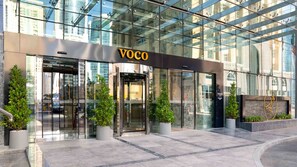 L’extérieur d’un hôtel moderne, avec une façade en verre, des portes automatiques et des plantes en pot.