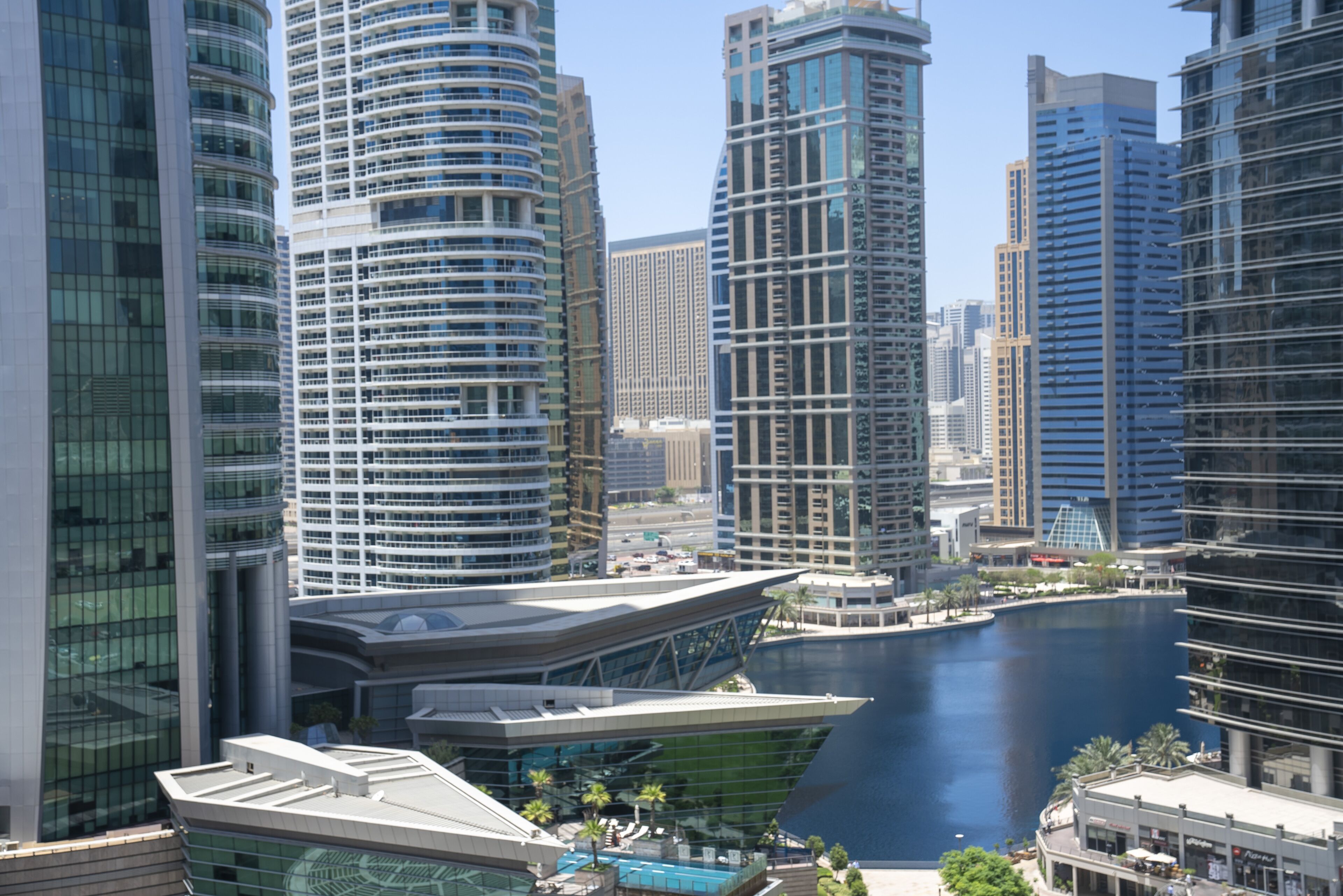 A modern cityscape with high-rise buildings, a waterfront, and a distinctive architectural structure with a curved roof.
