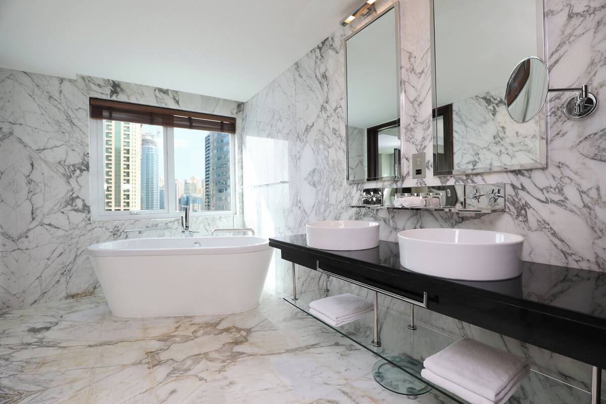 Ein modernes Badezimmer mit einer großen Badewanne, zwei Waschbecken, einem großen Spiegel und einem Fenster mit Blick auf die Stadt.