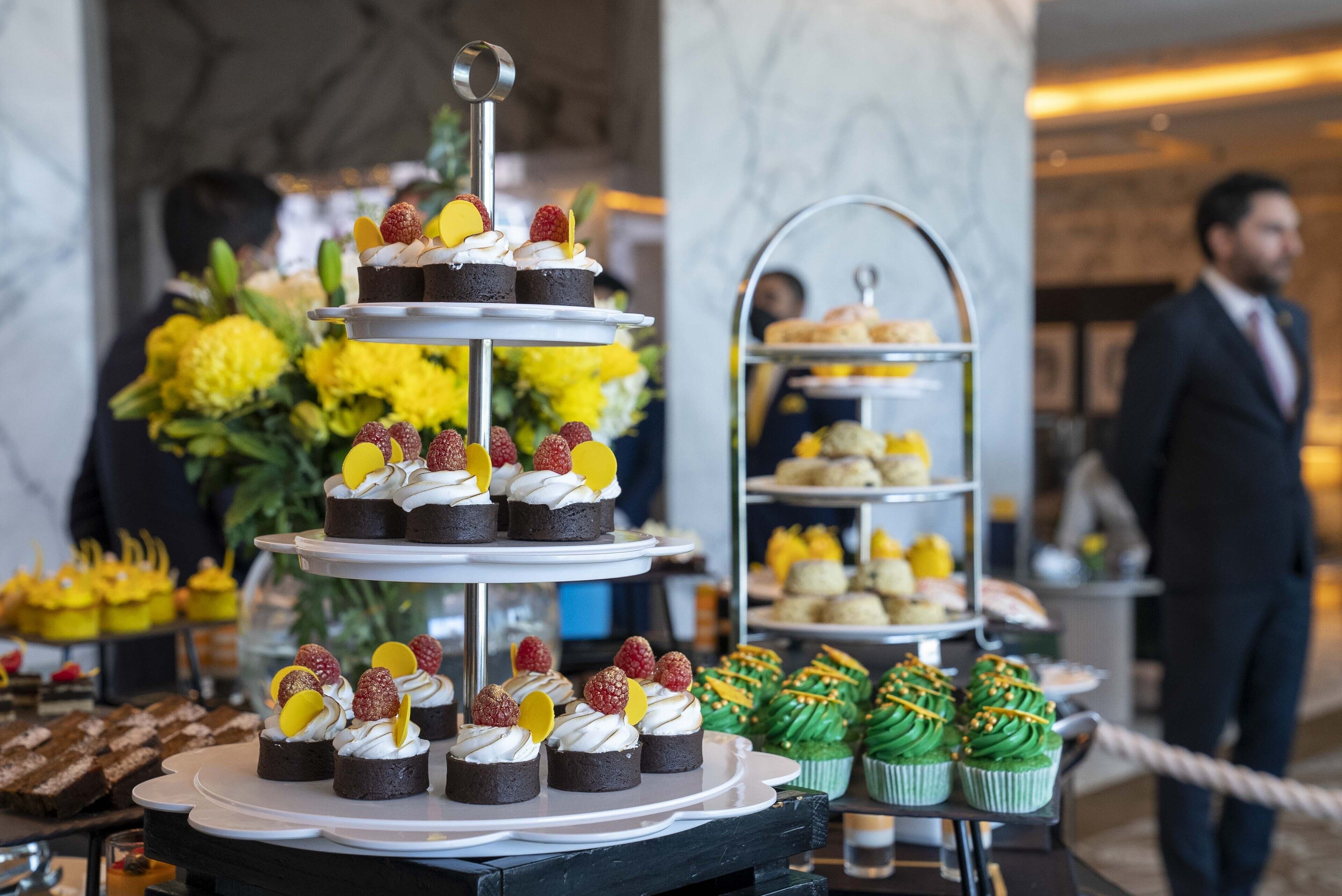 Eine mehrstufige Dessertpräsentation mit verschiedenen Gebäcken und Cupcakes, umgeben von gelben Blumen und weiteren Süßigkeiten.