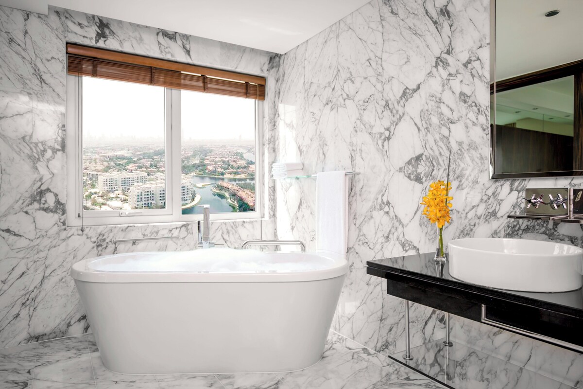 Ein modernes Badezimmer mit freistehender Badewanne, einem großen Fenster mit Blick auf die Stadt und einer Marmor-Spritzschutzwand.