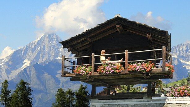 A wooden chalet with a balcony, surrounded by mountains and flowers. - Lifestyle & Spa Hotel Grächerhof (Graechen)