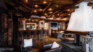 A cozy bar area with wooden beams, leather seating, and a stone fireplace. - Lifestyle & Spa Hotel Grächerhof (Graechen)